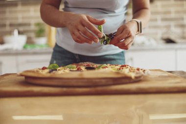 Geleneksel İtalyan pizzasına fesleğen yaprağı, yeşillik ekleyen kadın, mutfakta yemek pişiren kadın.