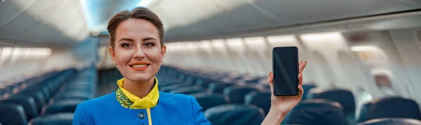 Радісна стюардеса зі смартфоном, що стоїть в салоні літака — стокове фото