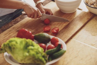 Bir tabak yeşilliğin yanında domatesleri tahta bir mutfak tahtasıyla doğrayan kadınların yakın çekimi.