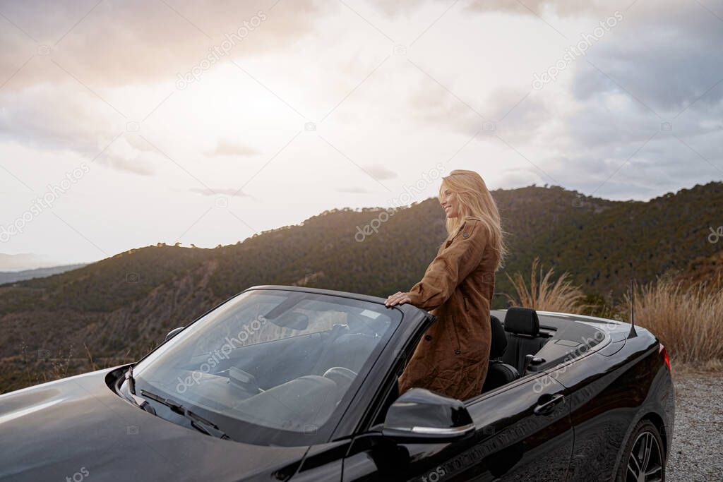 Smiling Caucasian female looking away enjoying panorama view from convertible car. Vacation concept