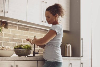 Güzel bayan kahvaltıda yeşil salata yaparken bilekliğini kullanıyor. Sağlıklı beslenme, sağlık.