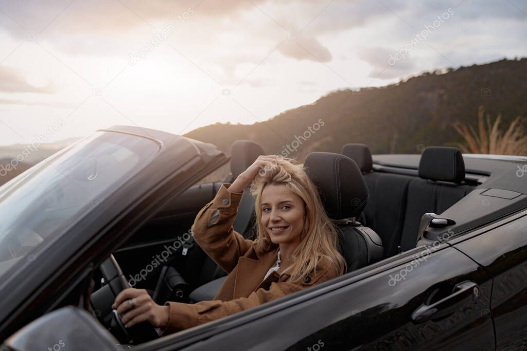 Close up portrait of cheerful young beautiful woman smiling to camera while driving a cabriolet car