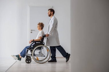 Tıp kliniğinde tekerlekli sandalyeli hasta taşıyan profesyonel bir erkek doktor. Yüksek kalite fotoğraf