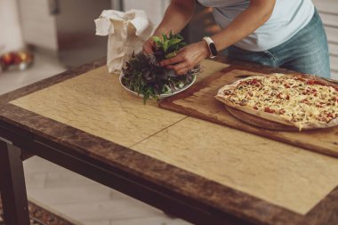Bir bayan fesleğeni alır ve pizzanın üstüne koyar. İtalyan pizza hazırlığı