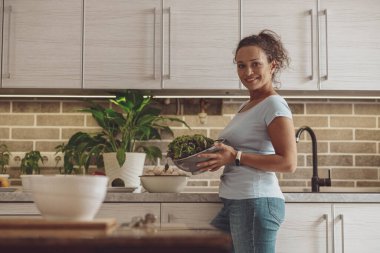 Fit bayan salatayla kaseyi tutarken evde lezzetli sağlıklı yiyecekler hazırlıyor.