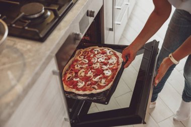 Ev yapımı İtalyan pizzası mutfaktaki kadın tarafından fırına konur.