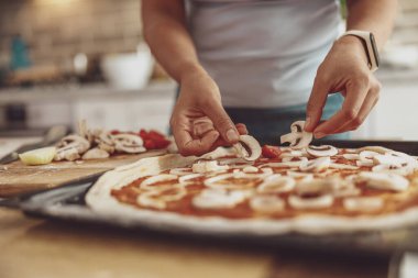 Bir kadın fırında pişirmeden önce ev yapımı pizzaya mantar sürer.