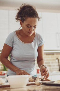 Tarz sahibi bir mutfakta genç bir kadın tarafından tahtada taze pizza mantarları dilimleniyor.