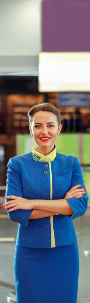 Cheerful stewardess in flight attendant uniform looking at camera and smiling while keeping arms crossed