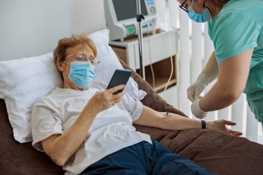 Hasta kıdemli hasta hastane koğuşunda tıbbi prosedür sırasında telefon kullanıyor. Yüksek kalite fotoğraf