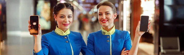 Radosne Stewardessy Mundurze Stewardessy Lotniczej Patrzące Kamerę Uśmiechnięte Trzymające Telefony — Zdjęcie stockowe