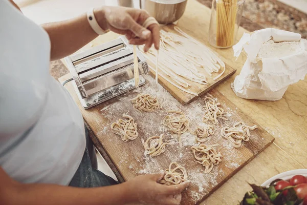 Bir kadın mutfak tahtasına makarna keskisiyle pişirilmiş erişte serer.
