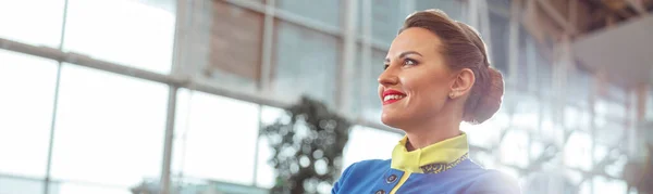 Cheerful woman stewardess in air hostess uniform looking away and smiling while keeping arms crossed