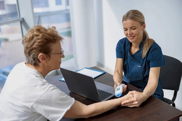 Doctor measures patients temperature with non-contact thermometer during an appointment in clinic