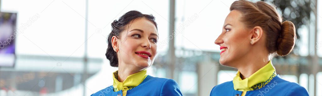 Cheerful woman stewardess in aviation uniform looking at colleague and smiling while waiting for the flight at airport