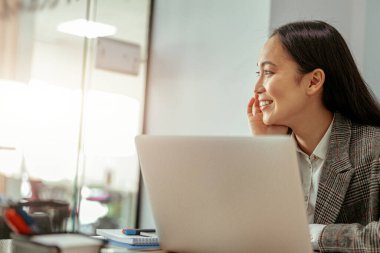 Ofiste çalışan yakışıklı Asyalı kadın gözlerini başka tarafa çeviren bir laptop kullanıyor. Bulanık arkaplan