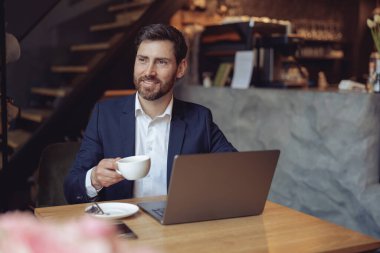 Çekici, zarif iş adamı elinde kahve fincanıyla kafeteryada dizüstü bilgisayara gülümsüyor. Portre.