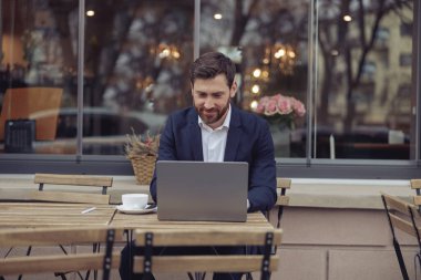 Beyaz tenli çekici iş adamı dışarıda, kafede dizüstü bilgisayarda çalışıyor. Klavyede mesaj yazıyorum. Çalışma konsepti.