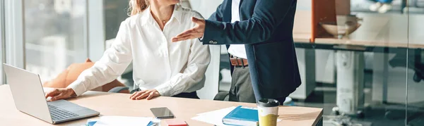 asian businessman is explaining plans to mature caucasian woman that working on laptop in office.