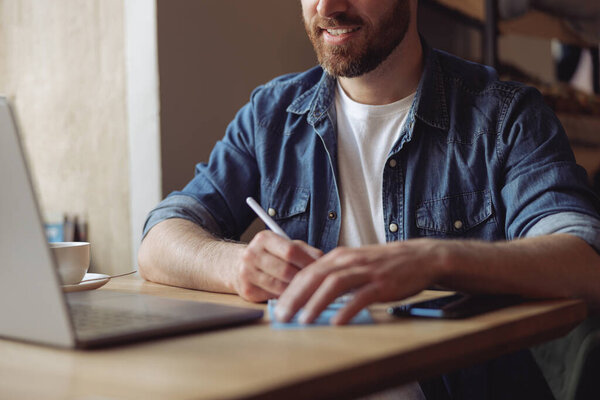 Hands of man with pen while taking notes at laptop. Work concept. Male noting at computer. Close up