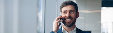 Gülümseyen işadamı ofiste çalışırken iş ortağını aramak için cep telefonu kullanıyor..