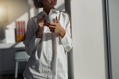 Close up of business woman holding cup of coffee and standing near window. Blurred background