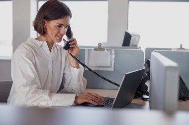 Smiling woman worker talk phone with client sit on her workplace in office. Blurred background