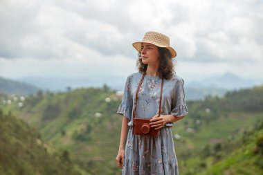 Happy young female traveler in hat with photo camera against of mountains in Africa
