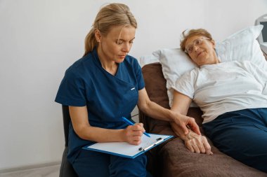Doctor measures patients heart rate and makes note in clipboard during treatment in a hospital ward