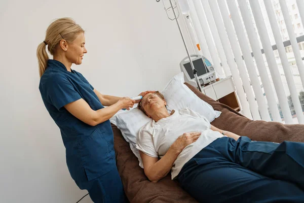 Doctor measures patients temperature with non-contact thermometer during treatment in hospital ward