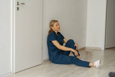 Tired nurse sits on floor in the lobby of medicine clinic after a hard shift. High quality photo