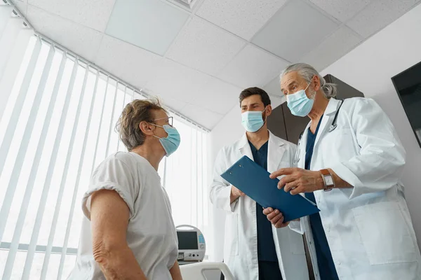 Doctors in masks explain to a sick patient in a wheelchair her diagnosis . High quality photo