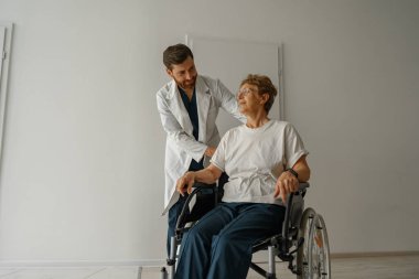 Klinikte tekerlekli sandalyeli hasta taşıyan profesyonel bir erkek doktor. Yüksek kalite fotoğraf