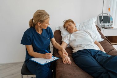 Doctor measures patients heart rate and makes note in clipboard during treatment in a hospital ward