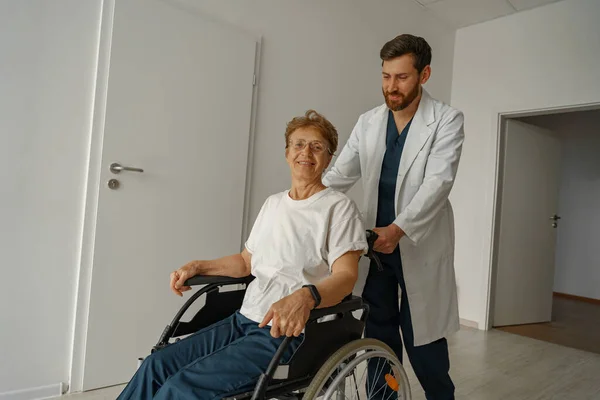 Профессиональный Врач Мужчина Несет Пациента Инвалидной Коляске Медицинском Зале Клиники — стоковое фото