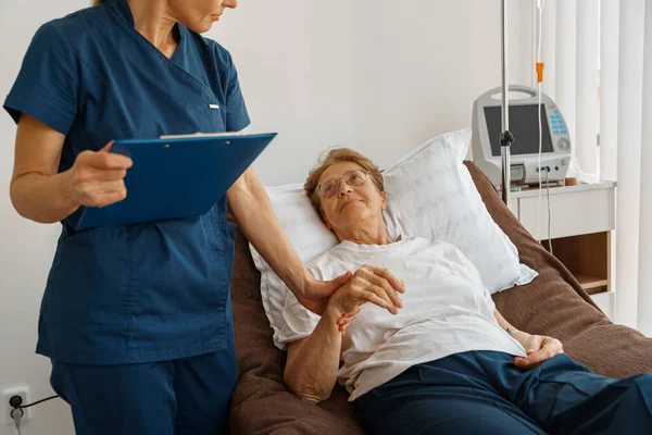 Doctor measures patients heart rate and makes note in clipboard during treatment in a hospital ward