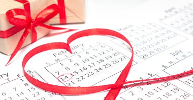 Calendar page with mark valentines day in red circle. February inside heart-shaped ribbon. Handmade gift box wrapped craft paper in the background. Horizontal banner, copy space.