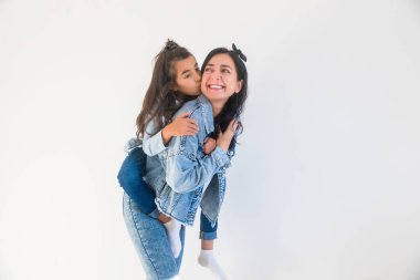 Küçük bir kız çocuğu annesini yanağından öpüyor, arkasından sarılıyor. Anneler Günü, mutlu annelik kavramı.