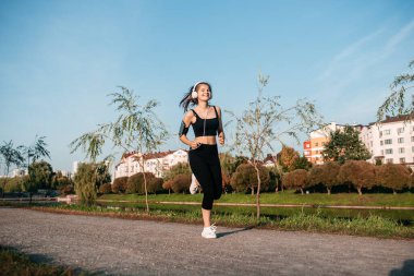 Kulaklık takan bir kız bir metropolde açık hava fitnesiyle meşgul. Koşu ve yaz sporları