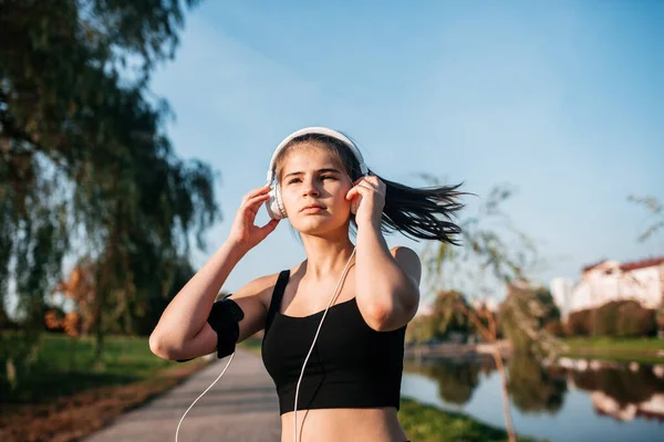 A girl in headphones is engaged in outdoor fitness in a metropolis. running and sports in summer Stock Photo