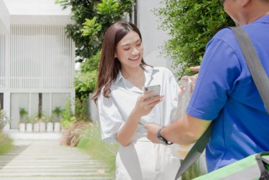 Teslimatçı, güzel bir Asyalı kıza evin önünde yemek getiriyor. ödemeler akıllı telefondan ulaşılamıyor, QR kodu taranıyor