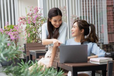 Asyalı kız dışarıda bayan arkadaşıyla çalışırken dizüstü bilgisayarına bakıyor..