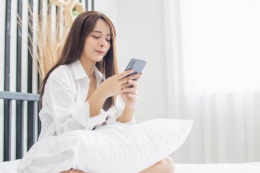 Portre genç gülümseme mutlu Asyalı kadın rahatla yatak odası. Kadınlar rahatlamak için akıllı telefon aletleri kullanır. Evden alışveriş yaparlar..