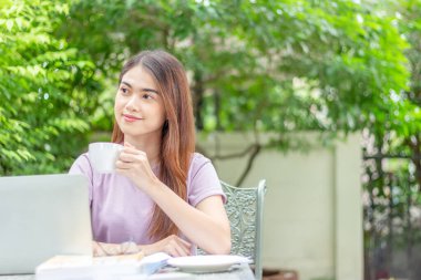 beauty woman doing freelance work in garden. Asian woman using laptop at home back yard with tree background copy space
