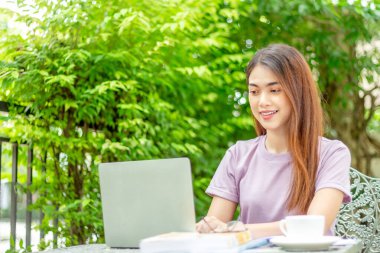beauty woman doing freelance work in garden. Asian woman using laptop at home back yard with tree background copy space