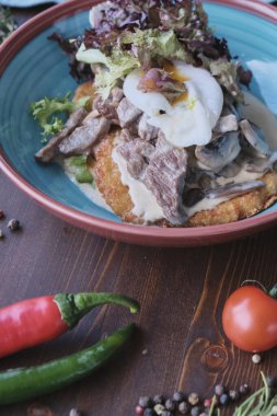 Tahta masada etli ve yumurtalı sıcak salata, gün ışığı.