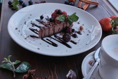 Nane ve böğürtlenle süslenmiş beyaz tabakta çikolatalı pasta.