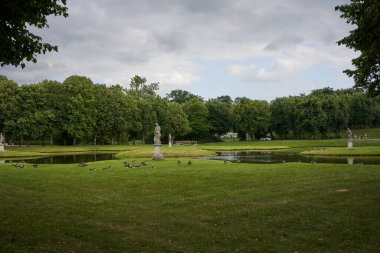 Schwerin, Almanya - 20 Temmuz 2021 - Bulutlu yaz akşamında heykelleri ve küçük köprüleri olan Castle Garden                               