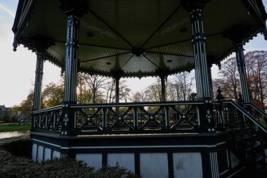Apeldoorn, Netherland - April 19, 2022 - Oranjepark: Music kiosk and bronze statue Man with flag in central park at the beginning of spring                                