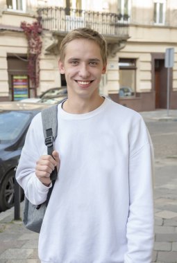 20-25 yaşlarındaki gülümseyen bir gencin sokak portresi omzunda sırt çantasıyla eski şehir mimarisinin arka planına yaslanmış. Belki de bilişim uzmanıdır ya da turist, öğrenci ya da acemi bir uzmandır..